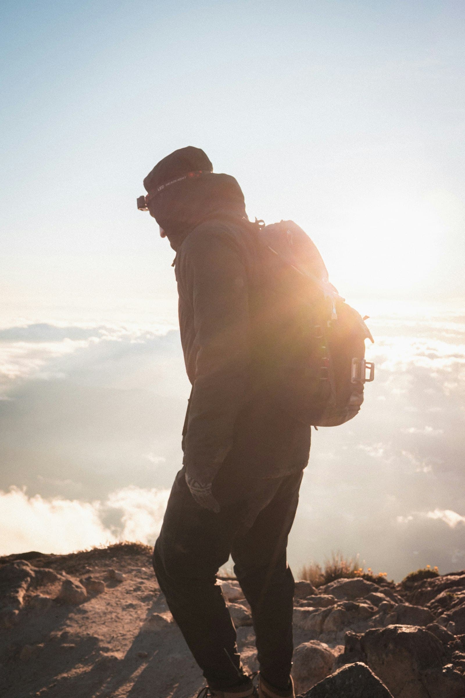 A hiker standing on a summit above the clouds, lit by the rising sun
